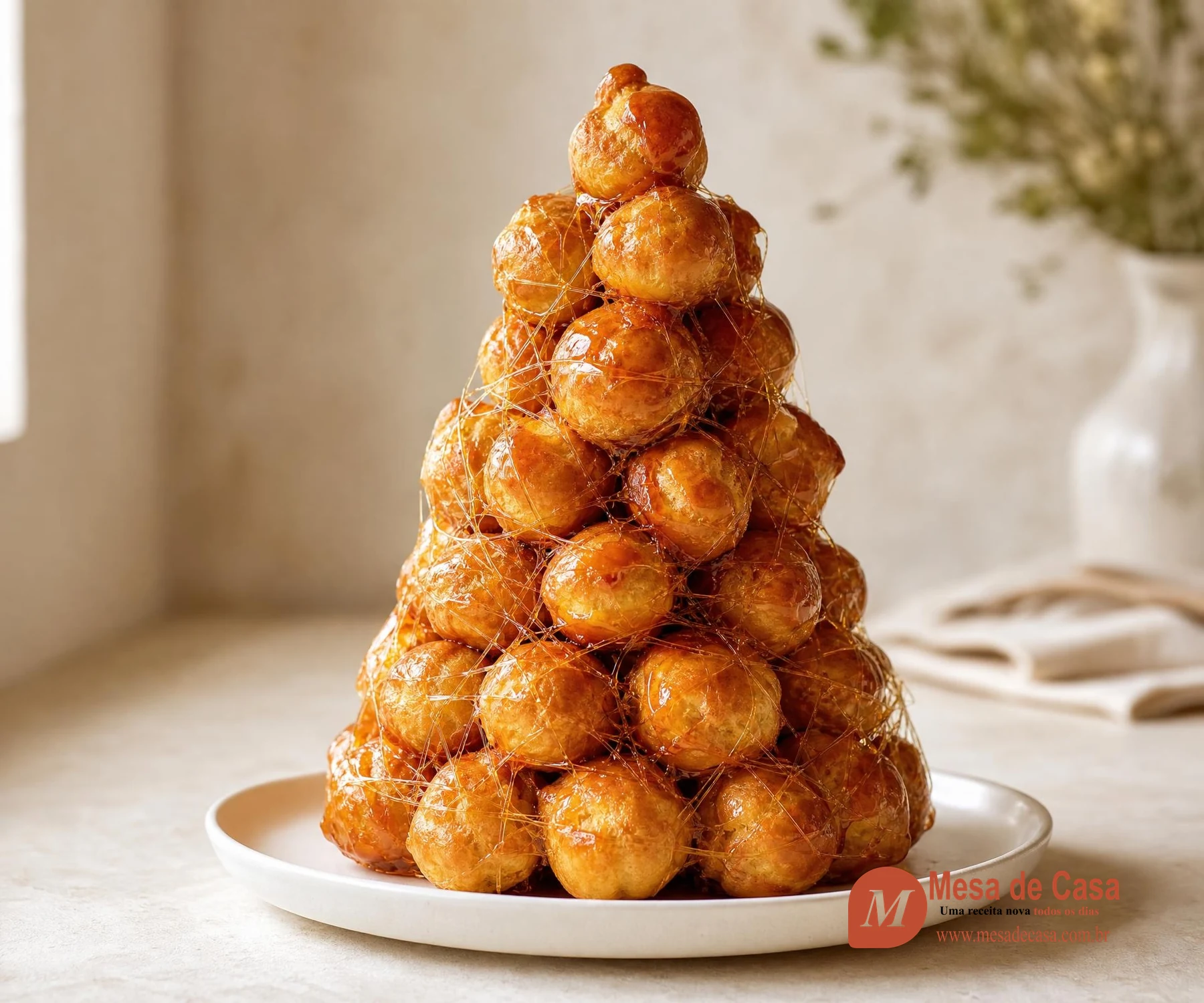 Torre de profiteroles dourados unidos por caramelo âmbar e envolvidos em fios delicados e brilhantes