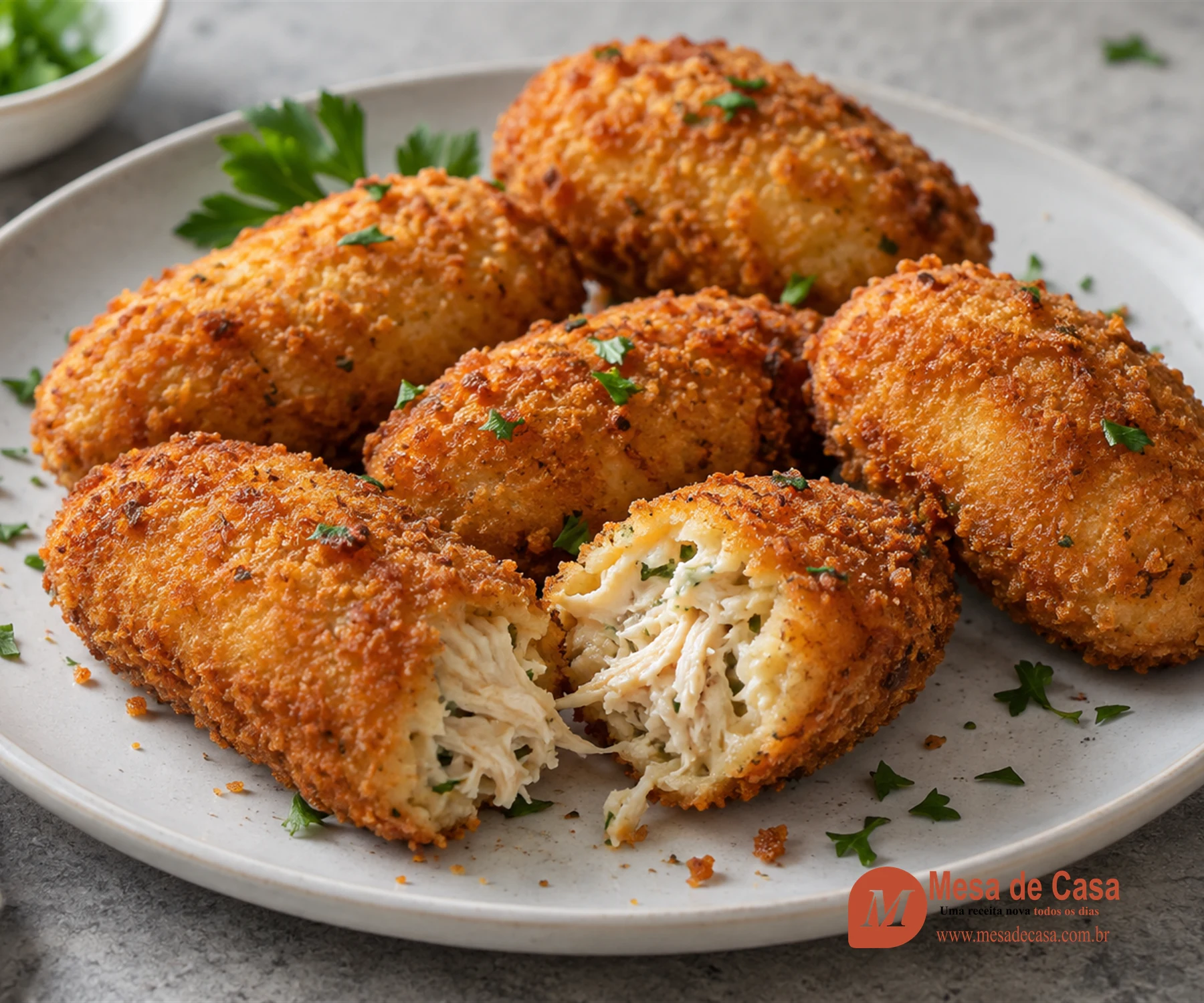 Croquetes de frango dourados, com um aberto revelando recheio cremoso e desfiado