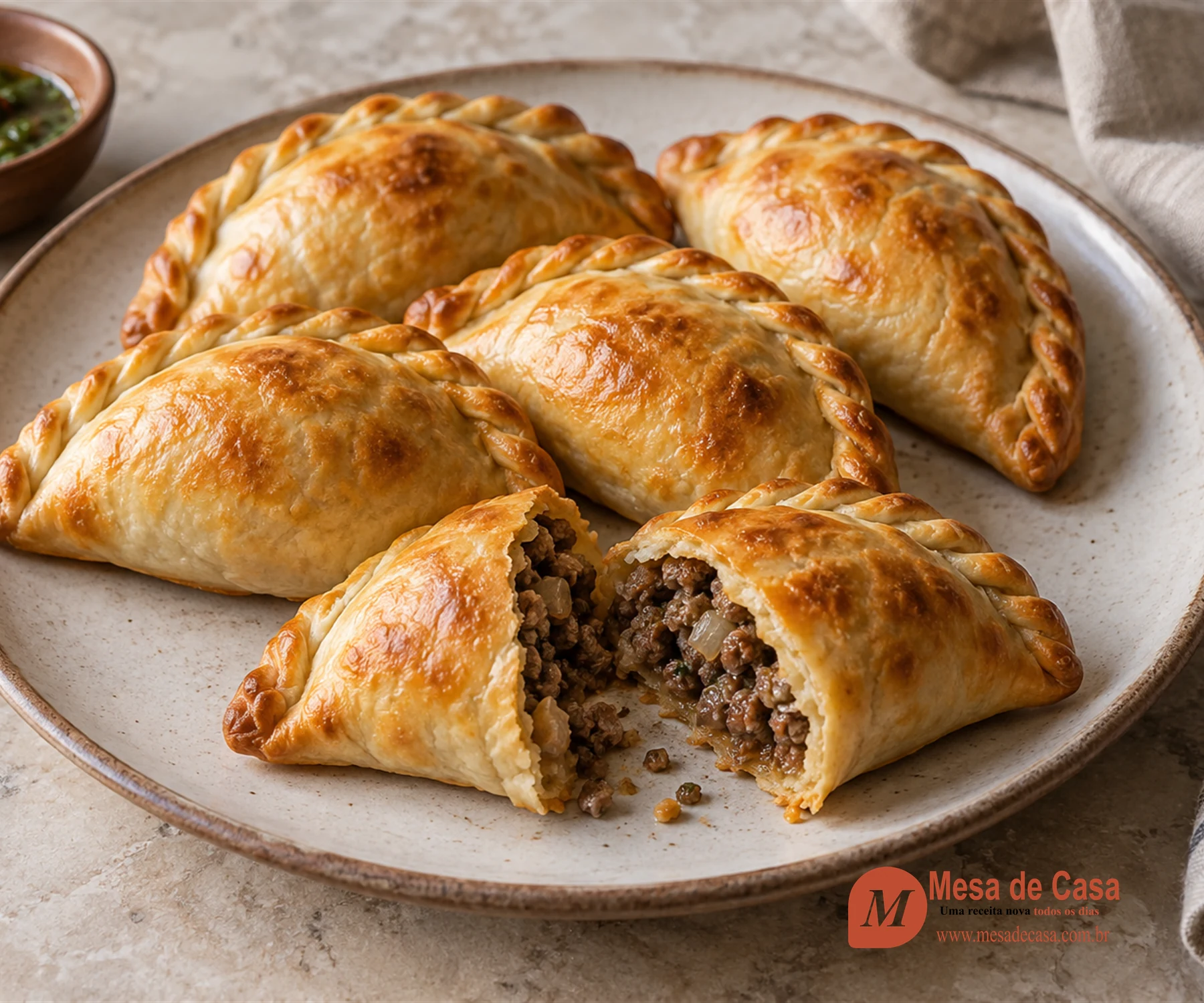 Empanadas argentinas douradas com repulgue trançado e recheio visível de carne e cebola